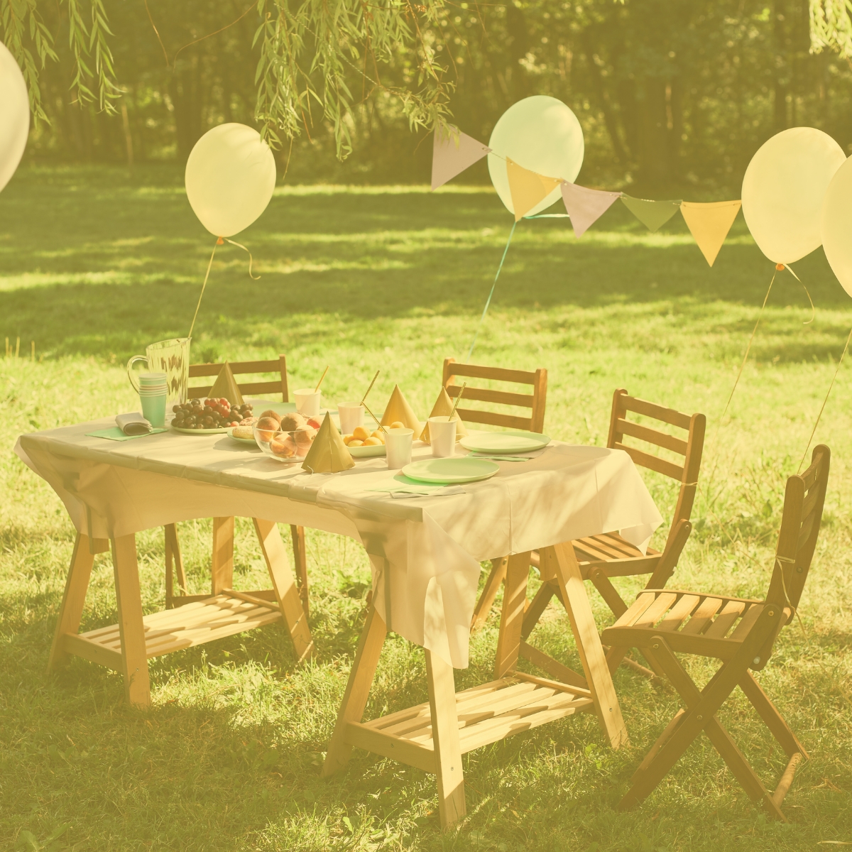 Gedeckter Tisch im Garten, geschmückt mit bunten Servietten und Luftballons für ein feierliches Kinderwillkommensfest. 